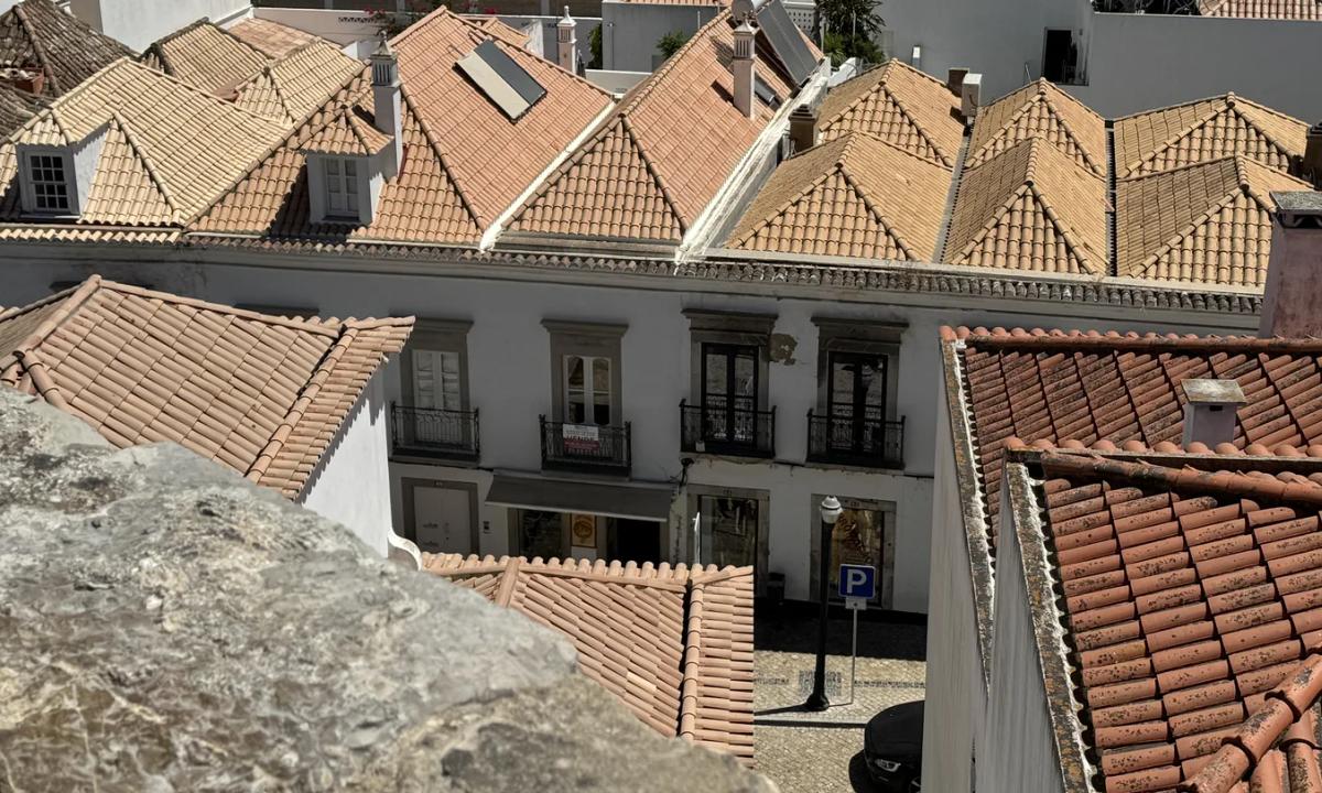 Tavira's roofscape seen from the castle: a row of small pyramid roofs, telhados de tesouro, above a white house façade. Own photo — Flemming Berthelsen, 2026.
