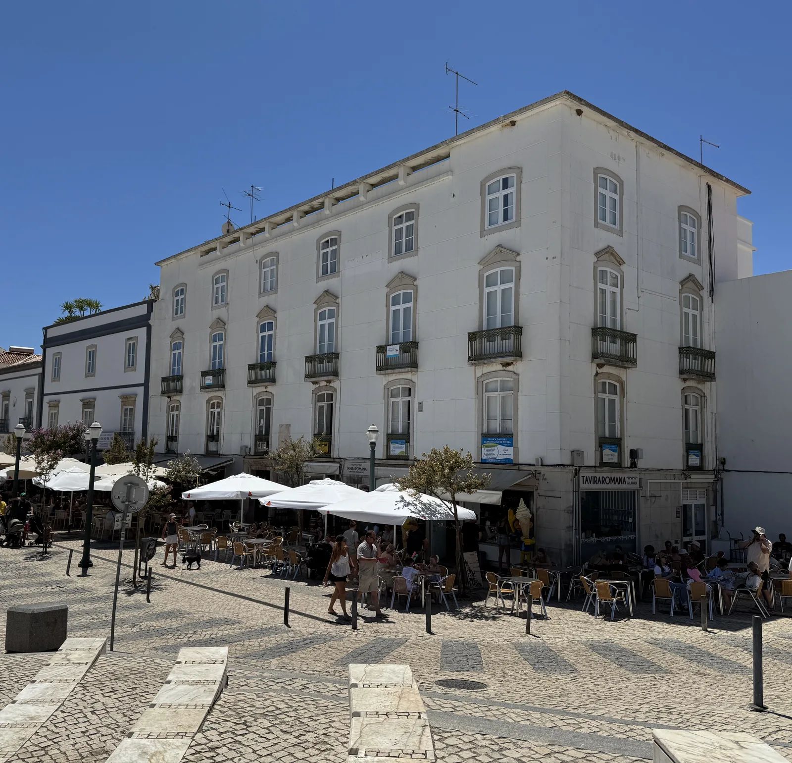 The row of houses on the Praça da República: four storeys with balconies and regular window bays above the café parasols. Own photo — Flemming Berthelsen, 2026.