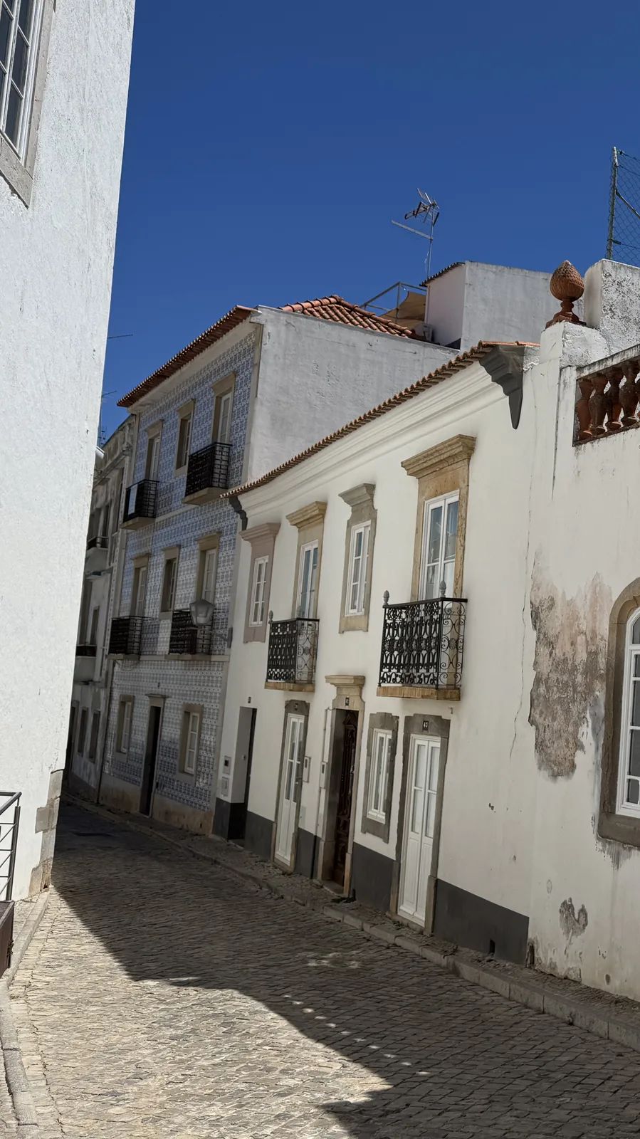 A narrow cobbled street by the church of Santiago: white façades with doors and single windows in rhythm down the street. Own photo — Flemming Berthelsen, 2026.