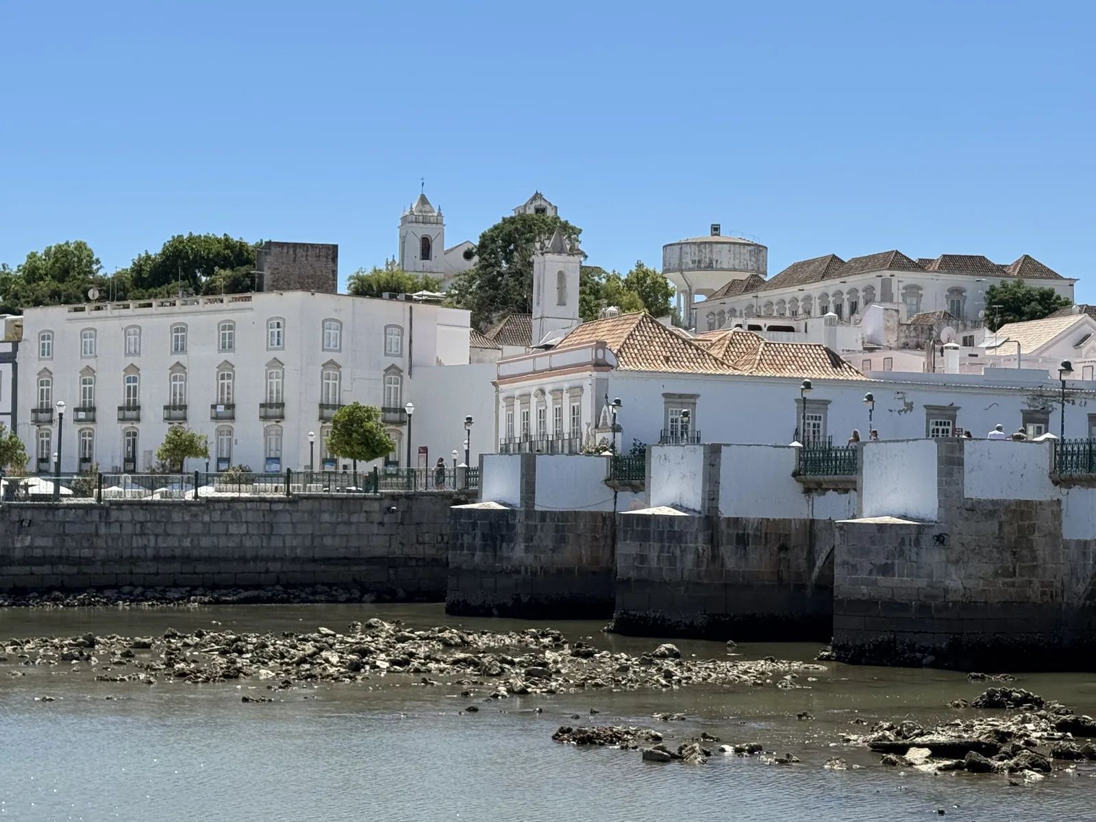 View from the other bank across the Gilão towards Tavira's white houses, the piers of the old bridge and the church towers on the hill. Own photo — Flemming Berthelsen, 2026.
